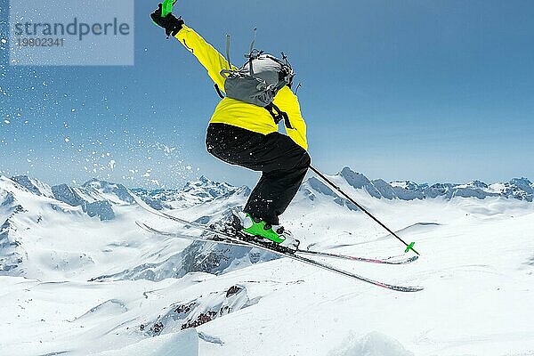 Ein Skifahrer in voller Sportausrüstung springt von der Spitze des Gletschers in den Abgrund  vor dem Hintergrund des blaün Himmels und der schneebedeckten Berge des Kaukasus. Blick von hinten. Elbrus Gebiet. Russland