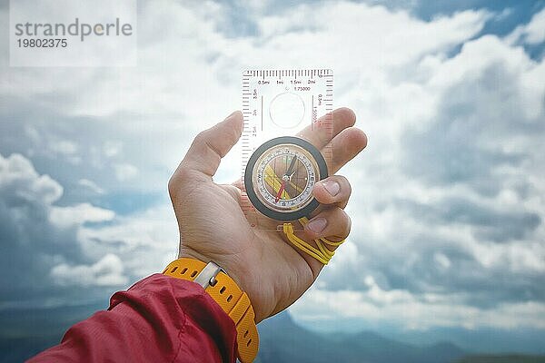 Männliche Hand hält einen magnetischen Kompass auf dem Hintergrund des Himmels mit Wolken. Das Konzept des Reisens und der Suche nach dem eigenen Lebensweg