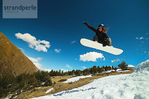 Stylish junges Mädchen Snowboarder macht den Trick beim Springen von einem Schnee Kicker gegen den blaün Himmel Wolken und Berge im Frühjahr. Das Konzept der Frühling Snowboarden in den Bergen und die Schließung der Winter Ski Saison