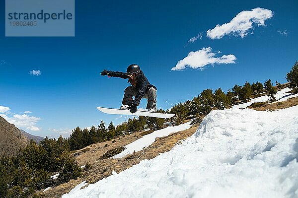 Stylish junges Mädchen Snowboarder macht den Trick beim Springen von einem Schnee Kicker gegen den blaün Himmel Wolken und Berge im Frühjahr. Das Konzept der Frühling Snowboarden in den Bergen und die Schließung der Winter Ski Saison