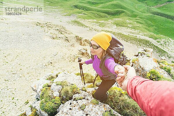 Ein Bergsteiger hilft einer jungen Bergsteigerin  den Gipfel des Berges zu erreichen. Ein Mann reicht einer Frau eine helfende Hand. Blick von oben