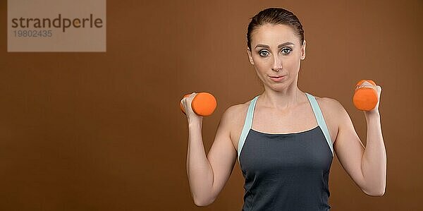 Porträt einer Frau Fitness Sportler Blick in die Kamera. Kaukasische Frau Fitness Sportler zeigt eine Geste der Stärke. Studio Foto. Auf einem braunen Hintergrund