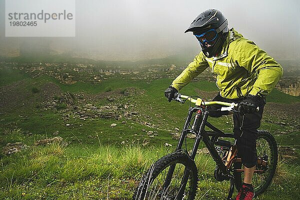 Ein Mann mit Berghelm und Mountainbike fährt bei bewölktem Wetter durch die schöne Natur bergab