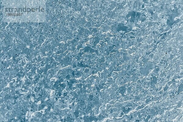 Nahaufnahme der Oberfläche eines Gletscherfragments mit einer Struktur aus Streifen und Blasen. Eisblaue Textur im Licht. Kleine Schärfentiefe
