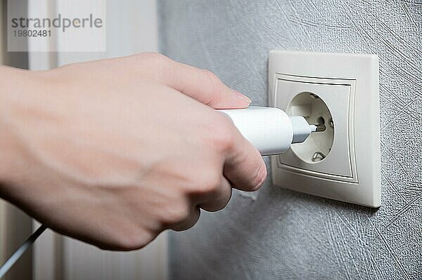 Nahaufnahme der Hand einer Frau  die ein weißes USB Ladegerät in eine 220 Volt Steckdose steckt