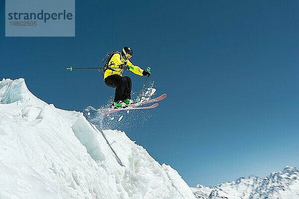 Ein Skifahrer in voller Sportausrüstung springt von der Spitze des Gletschers in den Abgrund vor dem Hintergrund des blaün Himmels und der schneebedeckten Berge des Kaukasus. Elbrus Gebiet. Russland