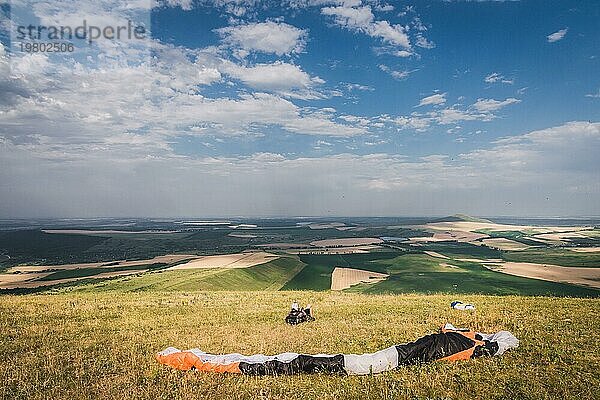 Ein professioneller Gleitschirmflieger in voller Ausrüstung und mit Helm liegt auf dem Gras hoch in den Bergen und schaut in die Wolken