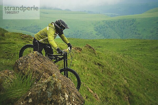 Ein Mann mit Berghelm und Mountainbike fährt bei bewölktem Wetter durch die schöne Natur bergab