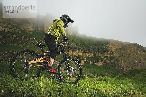 Ein Mann mit Berghelm und Mountainbike fährt bei bewölktem Wetter durch die schöne Natur bergab