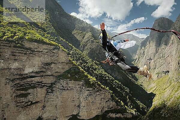 Ein Mann mit Helm springt mit einer leeren Flagge in den Bergen Seil hoch. Extremsportarten. Freizeit