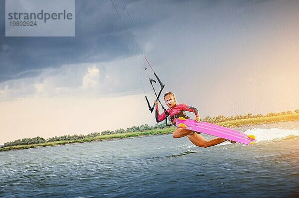 Eine junge Kitesurferin reitet auf den Wellen und zeigt einen Trick. Wassersport. Kitesurfen