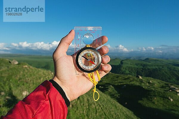 Mann auf der Suche nach der Richtung mit einem Kompass in der Hand in den sommerlichen Bergen Ansicht. Richtungssuche
