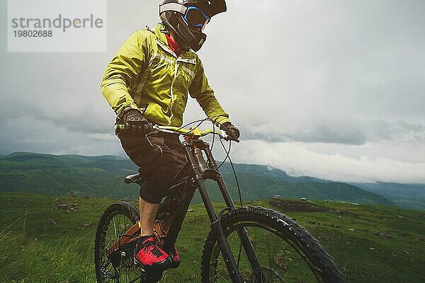 Ein Mann mit Berghelm und Mountainbike fährt bei bewölktem Wetter durch die schöne Natur bergab