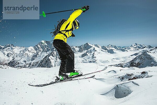 Ein Skifahrer in voller Sportausrüstung springt von der Spitze des Gletschers in den Abgrund  vor dem Hintergrund des blaün Himmels und der schneebedeckten Berge des Kaukasus. Blick von hinten. Elbrus Gebiet. Russland