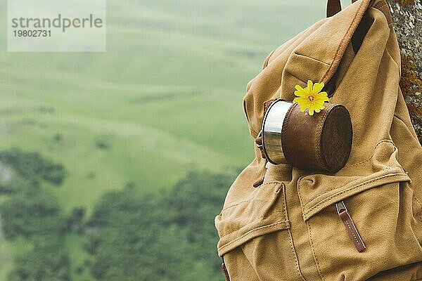 Hipster gelben Vintage Rucksack mit einem Becher auf sie mit einem Becher Nahaufnahme Vorderansicht befestigt. Traveler's Reisetasche im Hintergrund einer Berglandschaft