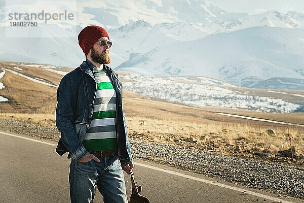 Porträt eines nachdenklichen stilvollen Hipsters mit Bart  Sonnenbrille und Hut mit einem Rucksack vor dem Hintergrund des schneebedeckten Berges Elbrus im Kaukasus bei Sonnenuntergang