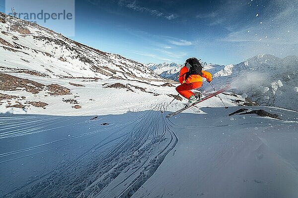 Ein männlicher Skisportler springt an einem sonnigen Tag von einem schneebedeckten Hang vor dem Hintergrund einer Berglandschaft mit schneebedeckten Bergen. Das Konzept des Wintersports