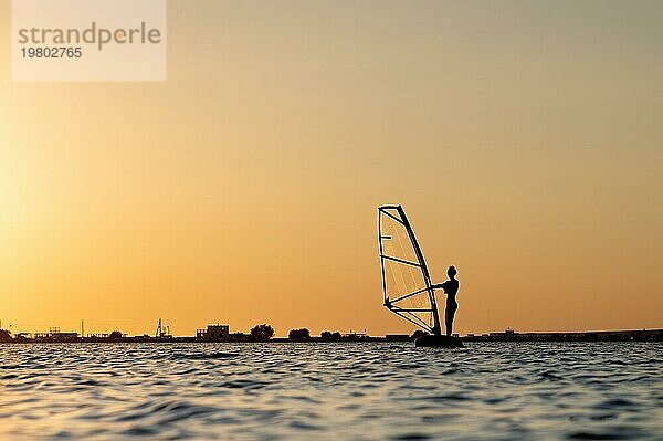 Silhouette einer jungen Kitesurferin bei Sonnenuntergang. Training bei ruhigem Wetter an der Flussmündung