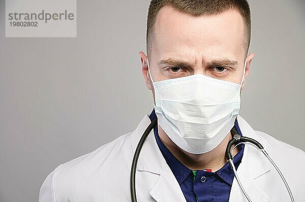 Der strenge Blick eines jungen Arztes mit Schutzmaske schaut mürrisch in die Kamera. Studioporträt