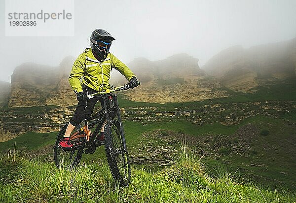 Ein Mann mit Berghelm und Mountainbike fährt bei bewölktem Wetter durch die schöne Natur bergab