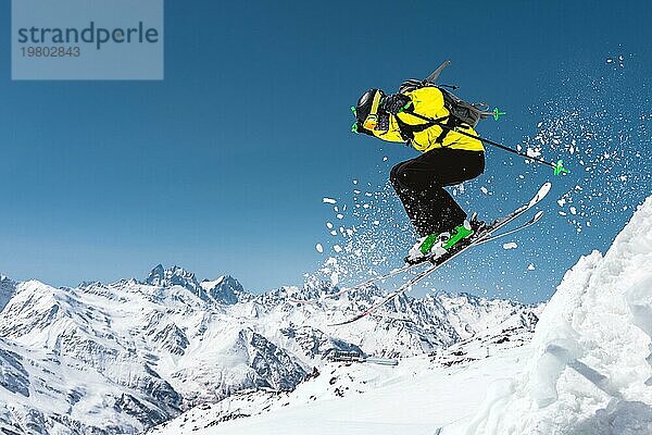 Ein Skifahrer in voller Sportausrüstung springt von der Spitze des Gletschers in den Abgrund vor dem Hintergrund des blaün Himmels und der schneebedeckten Berge des Kaukasus. Elbrus Gebiet. Russland