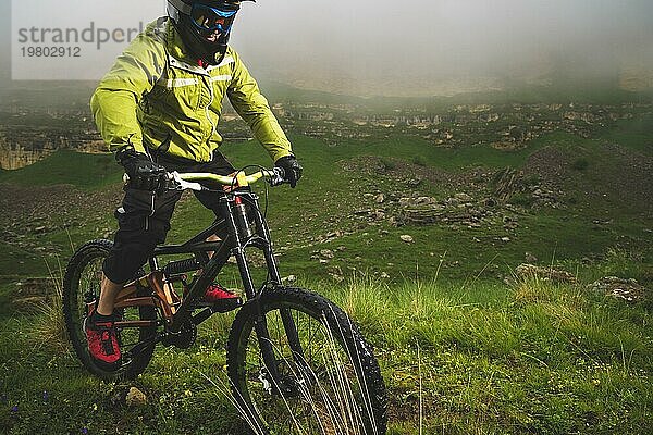 Ein Mann mit Berghelm und Mountainbike fährt bei bewölktem Wetter durch die schöne Natur bergab