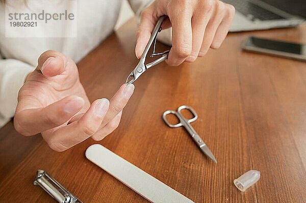 Junge kaukasische schöne Frau sitzt auf einem Stuhl in der Küche zu Hause  beschäftigt mit ihrer Schönheit Routine  räumt auf und Schönheit ihre Nägel auf ihre Hände während einer Maniküre. Parallele Kamerabewegung auf dem Schieberegler