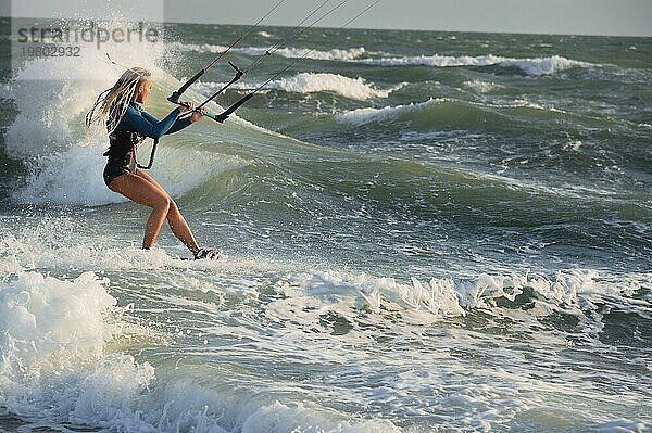 Professionelle Kitesurferin kaukasische Frau reitet große Wellen bei windigem Wetter. Kitesurfen