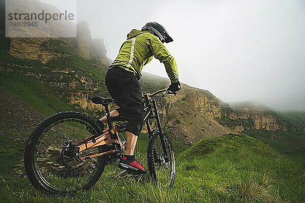 Ein Mann mit Berghelm und Mountainbike fährt bei bewölktem Wetter durch die schöne Natur bergab