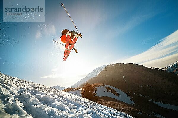 Mann Skifahrer im Flug nach dem Sprung von einem Kicker im Frühjahr vor dem Hintergrund der Berge und blaün Himmel. Nahaufnahme mit Weitwinkel. Das Konzept der Schließung der Skisaison und Skifahren im Frühjahr