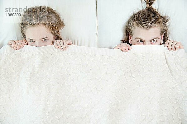 Ein junges Paar im Bett bedeckt die Hälfte seines Gesichts mit einer Decke und versteckt sich hinter einer Decke. Das Konzept der familienfreien Probleme und des Mangels an Dialog