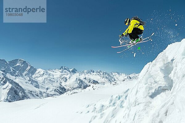 Ein Skifahrer in voller Sportausrüstung springt von der Spitze des Gletschers in den Abgrund vor dem Hintergrund des blaün Himmels und der schneebedeckten Berge des Kaukasus. Elbrus Gebiet. Russland