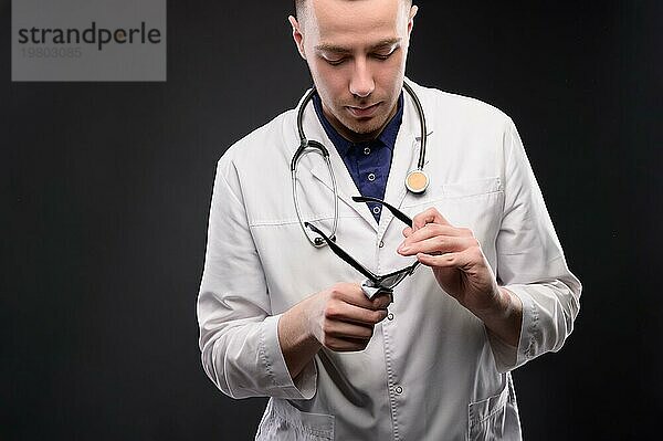 Porträt eines unglücklichen müden jungen Arztes mit Stethoskop und Kopfschmerzen auf dunklem Hintergrund. Probleme mit dem Arzt