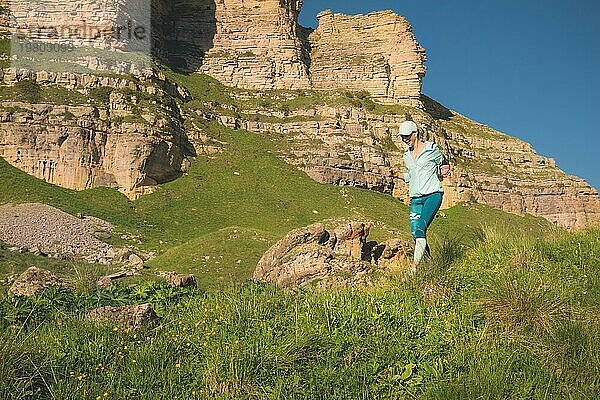 Attraktive Sportlerin mit Mütze und Kopfhörern joggt an einem malerischen Ort den Hügel hinunter in der Nähe der Felsen bei Sonnenuntergang. Workout im Freien
