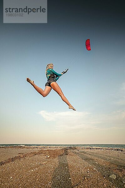 Sportliche Kitesurferin springt mit ihrem Lenkdrachen am Strand. Freier Flug über Land mit einem Drachen