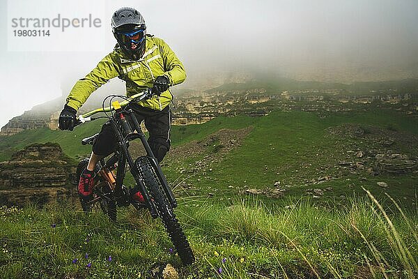 Ein Mann mit Berghelm und Mountainbike fährt bei bewölktem Wetter durch die schöne Natur bergab