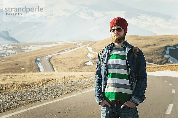 Porträt eines nachdenklichen stilvollen Hipsters mit Bart  Sonnenbrille und Hut mit einem Rucksack vor dem Hintergrund des schneebedeckten Berges Elbrus im Kaukasus bei Sonnenuntergang