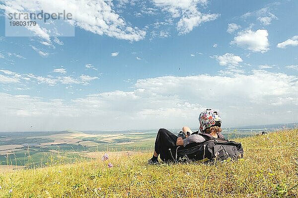 Ein professioneller Gleitschirmflieger in voller Ausrüstung und mit Helm liegt auf dem Gras hoch in den Bergen und schaut in die Wolken