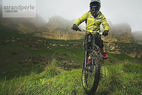 Ein Mann mit Berghelm und Mountainbike fährt bei bewölktem Wetter durch die schöne Natur bergab