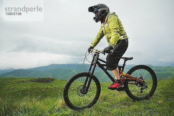 Ein Mann mit Berghelm und Mountainbike fährt bei bewölktem Wetter durch die schöne Natur bergab