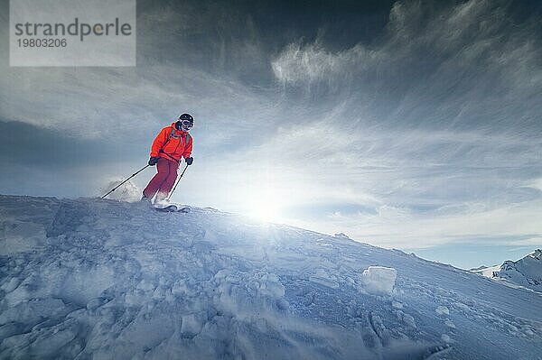 Ein männlicher Skisportler springt an einem sonnigen Tag von einem schneebedeckten Hang vor dem Hintergrund einer Berglandschaft mit schneebedeckten Bergen. Das Konzept des Wintersports