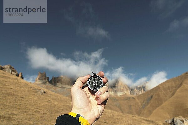 Ein männlicher Wanderer sucht mit einem Magnetkompass in den Bergen im Herbst nach einer Richtung. Aufnahme aus der Vogelperspektive. Männerhand mit Uhrenarmband hält einen Kompass