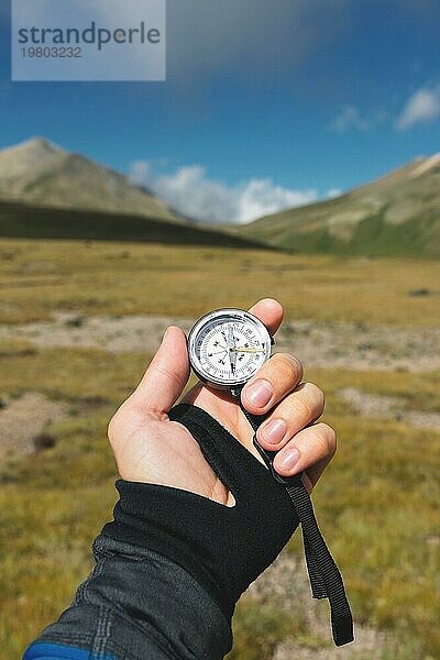 Blickpunktaufnahme. Eine Ichperspektive eines Mannes  der einen Kompass vor dem Hintergrund einer epischen Landschaft mit Klippen  Hügeln und einem blaün Himmel mit Wolken hält