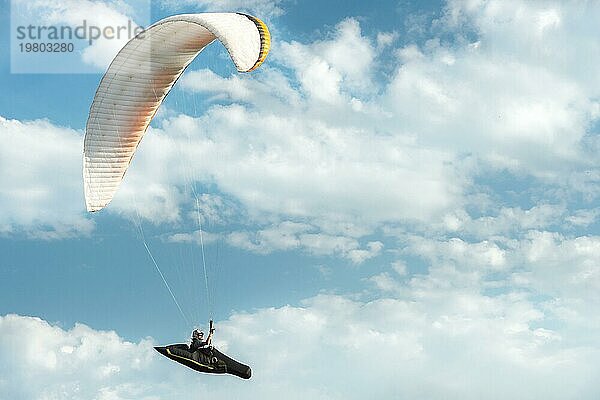 Professioneller Gleitschirmflieger fliegt mit einem weißen Gleitschirm gegen den blaün Himmel und die weißen Wolken. Gleitschirmfliegen Sport