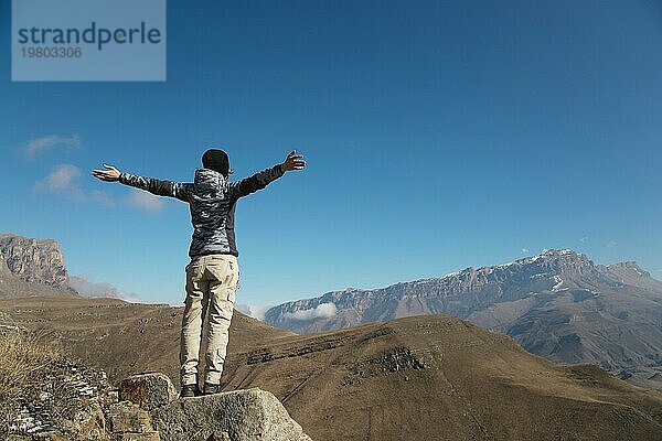 Der Applaus einer jungen Rucksacktouristin auf dem Gipfel eines sich ausbreitenden  ansteigenden Berges. Freiheit und Sieg vor dem Hintergrund von Bergen und blauem Himmel