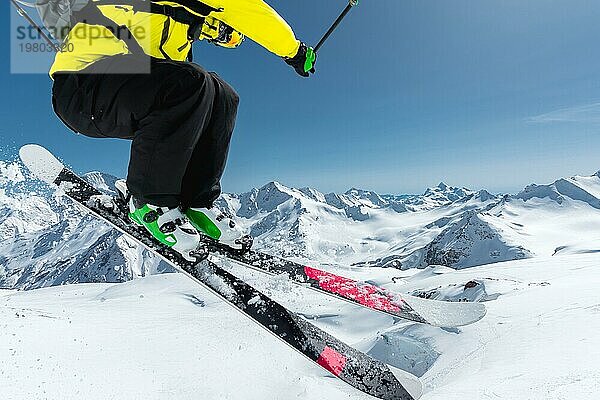 Ein Skifahrer in voller Sportausrüstung springt von der Spitze des Gletschers in den Abgrund  vor dem Hintergrund des blaün Himmels und der schneebedeckten Berge des Kaukasus. Blick von hinten. Elbrus Gebiet. Russland