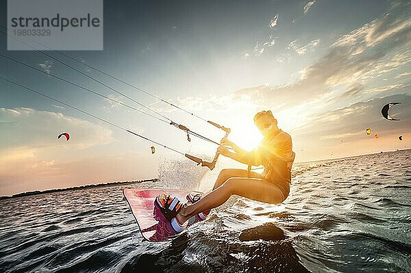 Professionelle Kitesurferin reitet auf einem Brett mit einer Planke in ihren Händen auf einem lemanischen See mit Meerwasser bei Sonnenuntergang. Wasser plätschert und Sonne blendet. Wassersport