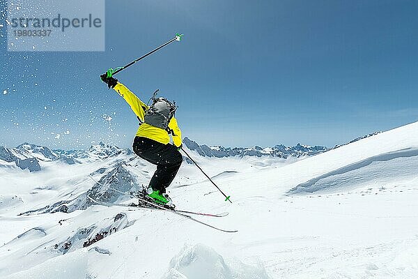 Ein Skifahrer in voller Sportausrüstung springt von der Spitze des Gletschers in den Abgrund  vor dem Hintergrund des blaün Himmels und der schneebedeckten Berge des Kaukasus. Blick von hinten. Elbrus Gebiet. Russland