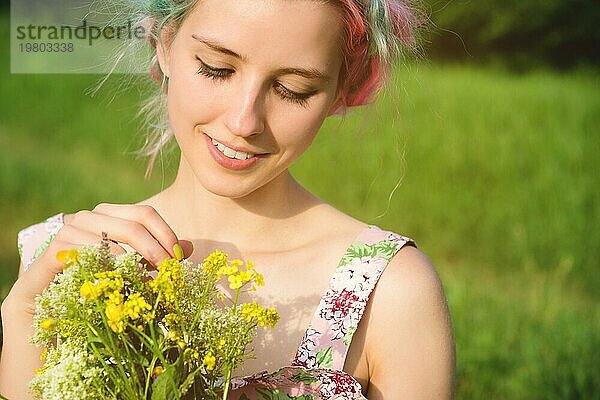 Porträt eines jungen  glücklich lächelnden Mädchens in einem Baumwollkleid mit einem Strauß Wildblumen