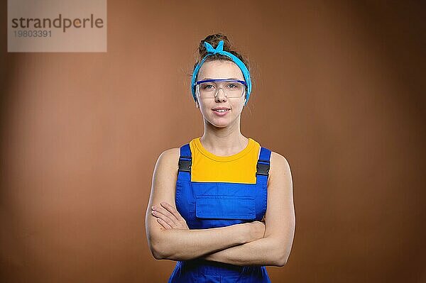 Porträt einer jungen Ingenieurin in blaür Uniform und mit Brille  Studioaufnahme auf braunem Hintergrund